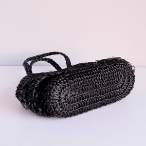 May include: A black woven handbag with braided handles. The bag has a rectangular shape with rounded edges. The material appears to be a tightly woven synthetic fibre, giving it a textured appearance. The bag is set against a white background.