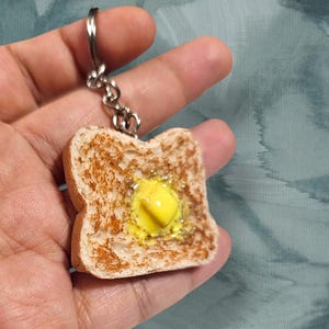 May include: A keychain shaped like a slice of toasted bread with a pat of yellow butter on top.