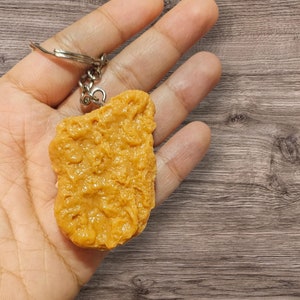 May include: A golden yellow chicken nugget keychain with a silver metal key ring.