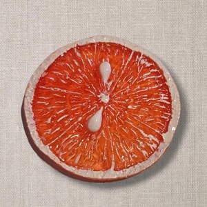 May include: A close-up of a bright orange ceramic grapefruit slice with white painted details. The slice is textured to resemble the inside of a grapefruit.