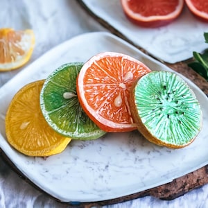 以下が含まれることがあります： 白い大理石の皿に、レモン、ライム、オレンジ、キウイの4種類の果物の輪切りが載っている。