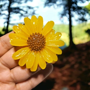 May include: A bright yellow sunflower with a brown center. The sunflower is made of resin and has a glossy finish.
