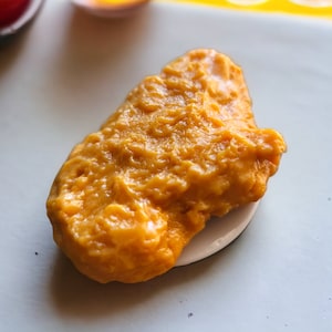 May include: A close-up of a single, golden-brown, fried chicken wing on a white plate.