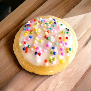 May include: A round, yellow sugar cookie with white frosting and colorful sprinkles.