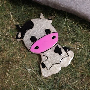 Puede incluir: Una vaca blanca brillante con manchas negras y una nariz rosa. La vaca está hecha de resina y tiene un acabado brillante.