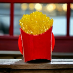 Puede incluir: Un contenedor de cartón rojo y blanco lleno de patatas fritas amarillas. El contenedor está sobre una superficie de madera.