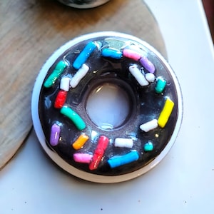 May include: A chocolate donut with colorful sprinkles. The donut is glazed and has a hole in the center.