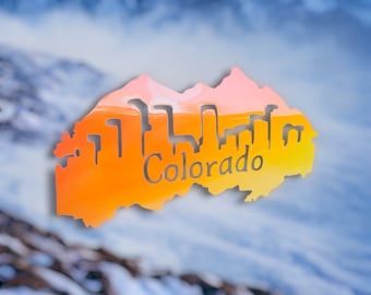 May include: An orange and pink silhouette of the state of Colorado with the word "Colorado" in the center, superimposed over a blurry image of snow-capped mountains.
