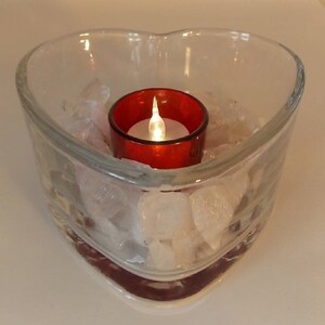 May include: A clear glass heart-shaped bowl filled with white rocks and a red votive candle holder with a white candle inside.