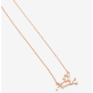 May include: A delicate rose gold necklace with a constellation pendant featuring a cluster of small sparkling stones. The necklace is a dainty and feminine piece of jewelry.