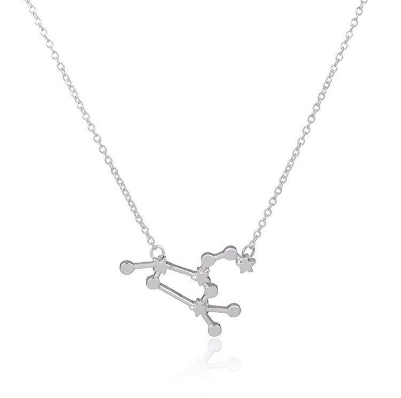 May include: A silver necklace with a delicate chain and a pendant shaped like the constellation Virgo. The pendant is made of small, interconnected circles and stars.