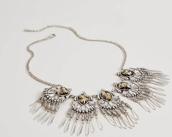 May include: A silver necklace with a black and gold pendant and multiple silver fringe strands.