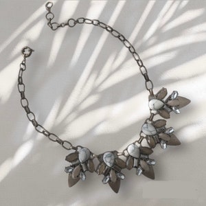 May include: A silver chain necklace with a white and gray stone pendant. The pendant is made up of several smaller stones arranged in a floral pattern.