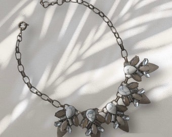 May include: A silver chain necklace with a white and gray stone pendant. The pendant is made up of several smaller stones arranged in a floral pattern.