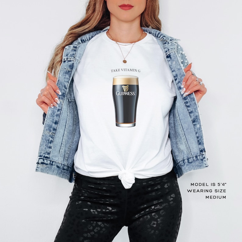 Puede incluir: Camiseta blanca con un gr&aacute;fico de vaso de pinta Guinness negro y dorado y el texto "Take Vitamin G".