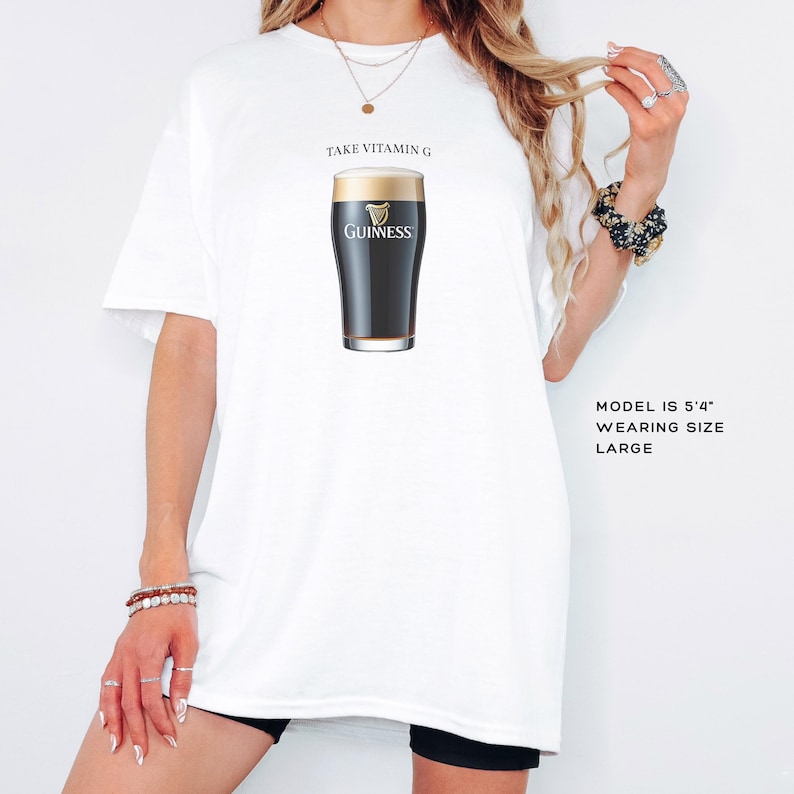 Puede incluir: Camiseta blanca con el texto "Take Vitamin G" y un gr&aacute;fico de un vaso de cerveza Guinness. La modelo lleva una talla grande.