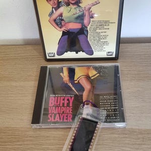 Puede incluir: Una cinta VHS y una caja de CD para la película "Buffy, la cazavampiros". La portada de la cinta VHS presenta un fondo amarillo con el título "Buffy Der Vampir-Killer" y una foto del personaje principal sosteniendo una estaca. La caja del CD presenta una foto del personaje principal sosteniendo una estaca y el título "Buffy, la cazavampiros".