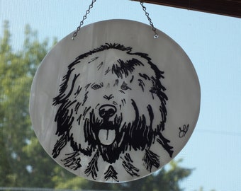 May include: A black and white illustration of a dog's head on a white circular glass ornament. The dog has a long, shaggy coat and is looking directly at the viewer with its tongue sticking out.