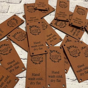 May include: A pile of brown leather labels with the text "Emily's Knits" and "Hand wash cold, dry flat" printed on them.
