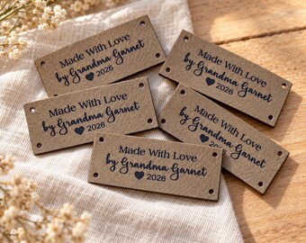 May include: Five rectangular tan labels with dark blue text reading Made With Love by Grandma Garnet and the year 2026 with a heart icon. Each label features four small pre-punched holes in the corners for attachment to handmade items.