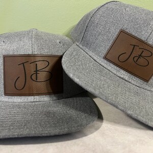May include: Two gray baseball caps with brown leather patches that have the initials "JB" in black script.