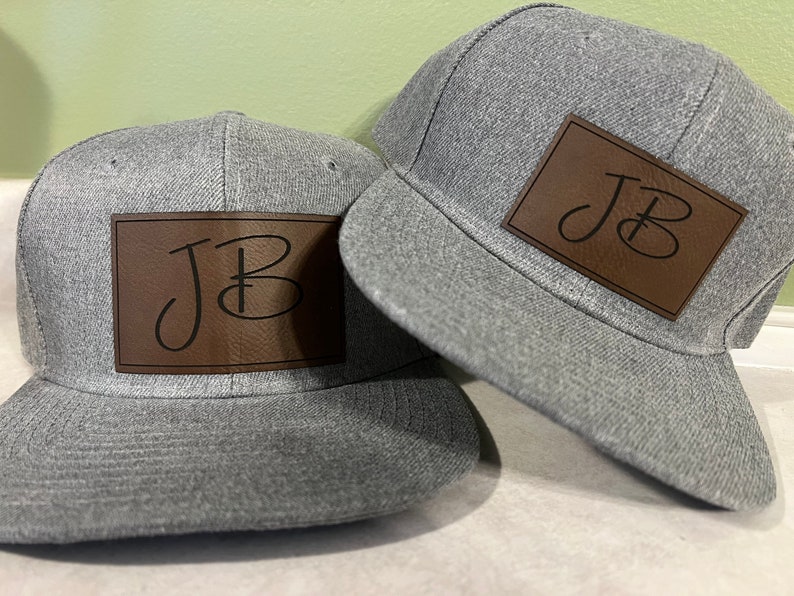 May include: Two gray baseball caps with brown leather patches that have the initials "JB" in black script.