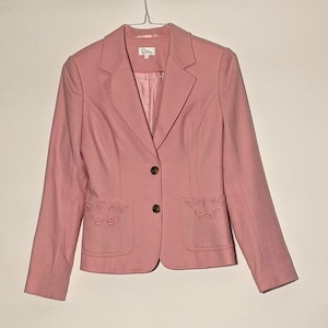 May include: A pink blazer with a button closure and two pockets. The pockets have embroidered butterfly designs.