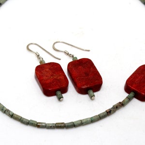 May include: A red coral necklace and earrings set with green turquoise beads. The necklace is made of small, round beads and the earrings are dangle style with square red coral stones.