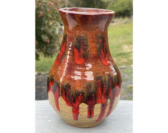 Puede incluir: Un jarrón de cerámica hecho a mano con un acabado brillante. El jarrón presenta una base marrón con patrones rojos y negros en forma de goteo. El borde superior es de color marrón oscuro. Jarrón decorativo con abertura acampanada.