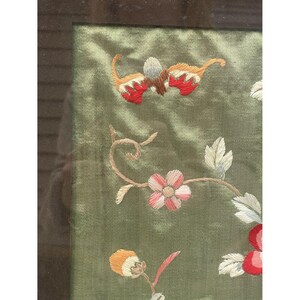 May include: A framed green silk embroidery with floral designs in shades of pink, red, orange, and white. The embroidery features a delicate floral pattern with leaves and flowers.