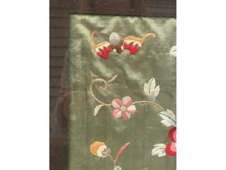 May include: A framed green silk embroidery with floral designs in shades of pink, red, orange, and white. The embroidery features a delicate floral pattern with leaves and flowers.