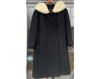 May include: A black double-breasted coat with a white faux fur collar. The coat has a ribbed texture and is lined with a black fabric.