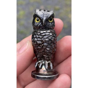 May include: A silver owl salt and pepper shaker with yellow eyes. The owl is perched on a round base.