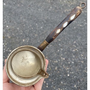 Puede incluir: Una cafetera turca de plata con un mango de madera incrustado con nácar. El mango tiene un lazo en la parte superior.