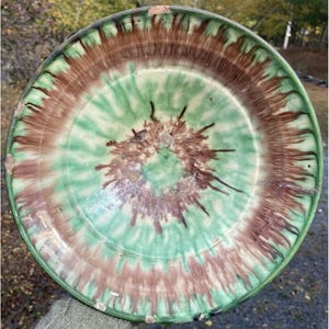 May include: A large, round ceramic plate with a green and brown glaze. The glaze is applied in a swirling pattern, creating a unique and rustic look.
