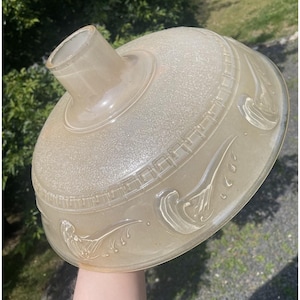May include: A translucent, light beige glass lamp shade with a dome shape and a central opening. The surface features a textured finish, a repeating geometric Greek key border pattern, and embossed floral motifs around the lower edge.