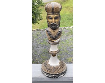 May include: A vintage, bronze-toned bust of a king wearing a crown, mounted on a white and bronze pedestal. The bust features a detailed face with a beard and regal attire. The pedestal has ornate detailing and measures approximately 76 cm in height.
