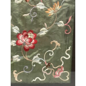 May include: A green fabric with embroidered flowers in shades of pink, red, and white. The flowers are arranged in a floral pattern with delicate vines.
