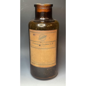 Könnte beinhalten: Eine braune Glasflasche mit einem Etikett mit der Aufschrift "Potassium Oxalate C.P. K2C2O4.H2O" und einem kleineren Etikett mit der Aufschrift "Schering's".