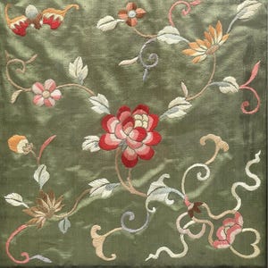 May include: A green fabric with embroidered floral designs in shades of pink, red, white, and yellow. The flowers are arranged in a repeating pattern on the fabric.