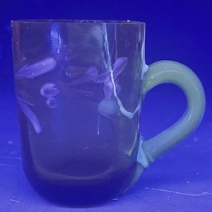 May include: A clear glass mug with a light blue handle and a purple floral design. The mug has a rounded shape and a wide base.