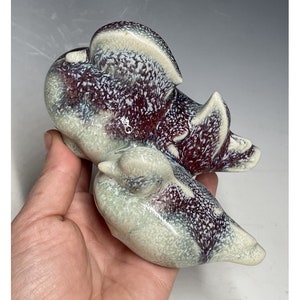 May include: A ceramic sculpture of two birds, one perched on top of the other. The birds are painted in shades of white, gray, and burgundy with a speckled glaze.