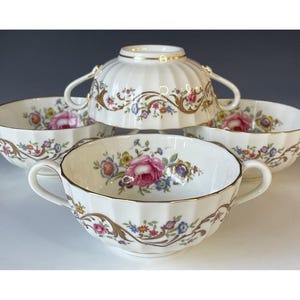 Puede incluir: Un juego de cinco cuencos de sopa de porcelana blanca con asas dobles, con un diseño floral con rosas rosas, flores azules y amarillas y ribete dorado. Los cuencos están apilados, mostrando los intrincados detalles de la vajilla vintage.