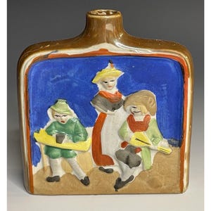 May include: A brown ceramic bottle with a blue and white scene of three people in traditional clothing. The bottle has a square shape and a wide mouth.