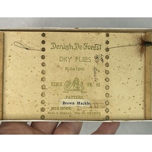 May include: A vintage box of Derwyn De Forest dry flies, labelled "Floating" and "Brown Hackle". The box is made in England and has a stock number of 65.