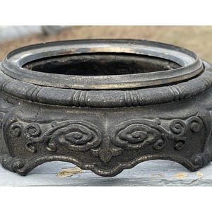 Może przedstawiać: Czarna żeliwna podstawa z ozdobnymi wzorami kwiatowymi. Podstawa ma okrągły wierzchołek i szeroką, rozszerzającą się podstawę.