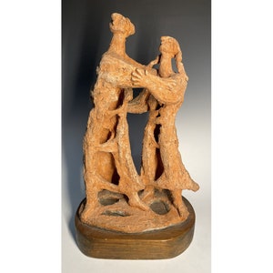 May include: A terracotta sculpture of two figures embracing. The figures are stylized and have a rough, textured surface. The sculpture is mounted on a wooden base.
