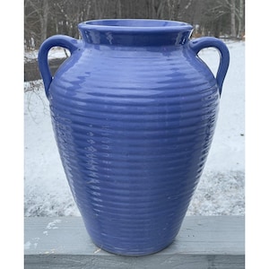 Op de afbeelding: Een grote, blauwe keramische vaas met twee handvatten. De vaas heeft een brede, geribbelde body en een licht uitlopende rand. De vaas is ongeveer 61 cm hoog.