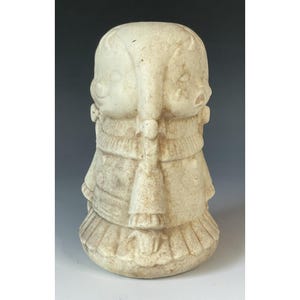 Könnte beinhalten: Eine cremefarbene Skulptur im Vintage-Stil, die zwei Kinder zeigt, die in entgegengesetzte Richtungen blicken. Die Skulptur weist detaillierte Kleidung und Frisuren mit einer strukturierten Oberfläche auf. Der Sockel ist rund, und das Gesamtdesign ist symmetrisch.