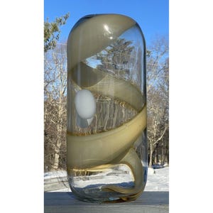 May include: A clear glass vase with a swirling pattern of beige and brown glass. The vase has a white orb inside.